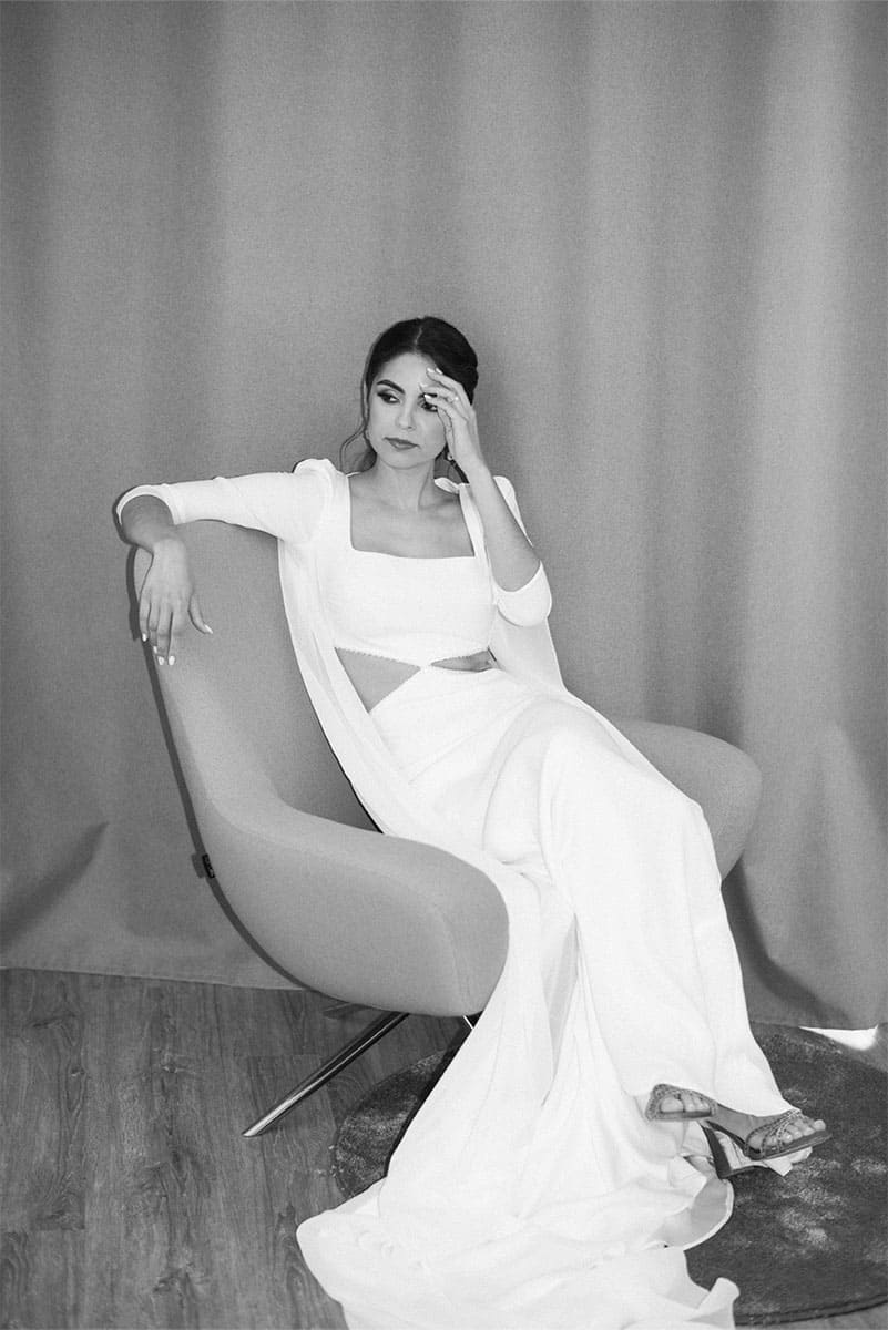 A woman in a flowing white dress sits elegantly on a modern chair