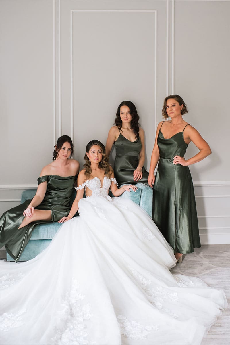 Una novia en un vestido de boda blanco con detalles de encaje se sienta junto a sus damas de honor